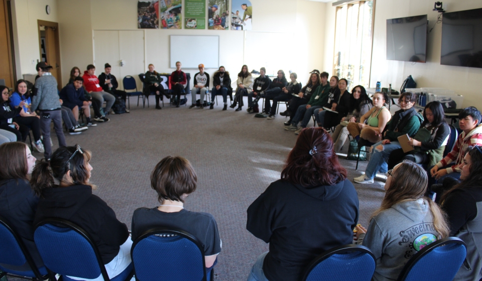 A large group of students are sitting in a circle inside of a conference room at Cal Poly Humboldt.